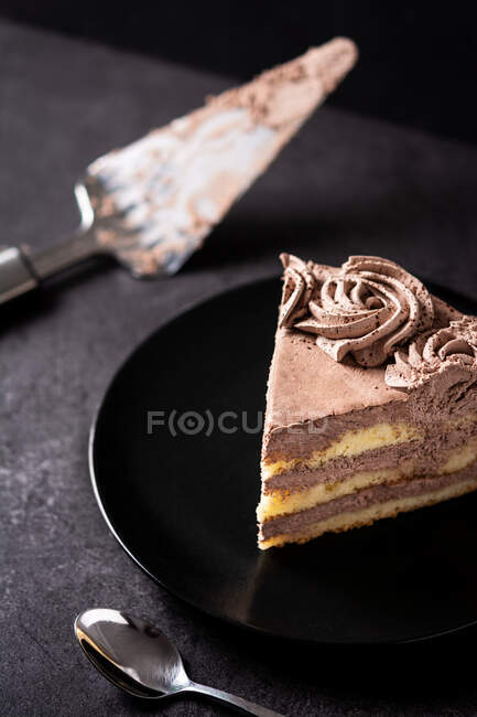 Dall'alto di pezzo di deliziosa torta al cioccolato al tartufo servita in piatto su tavolo nero con cucchiaio e spatola — Foto stock