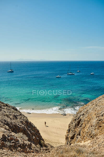 Playa con veleros al fondo sobre un mar turquesa bajo un cielo con nubes en el soleado día de verano en Fuerteventura, España - foto de stock