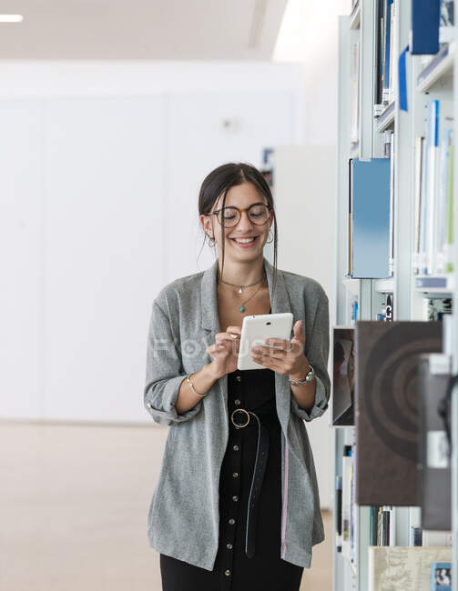 Femme dans des lunettes utilisant la tablette tout en se tenant debout dans un lieu de travail spacieux et travaillant sur le projet — Photo de stock