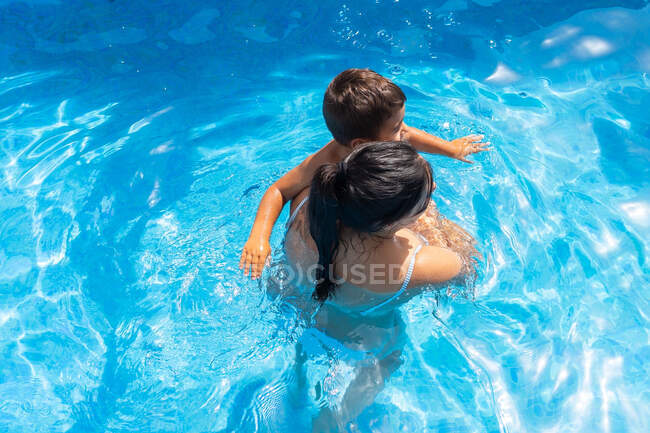 Top view of unrecognizable mother with son standing in swimming pool on sunny summer day — Stock Photo