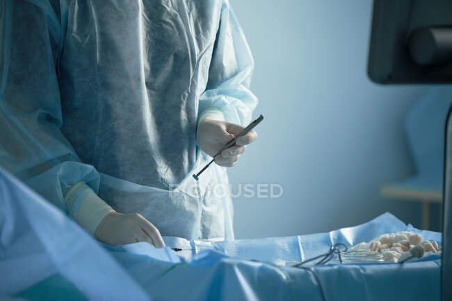 Cosecha enfermera irreconocible en uniforme estéril preparando instrumentos médicos para la cirugía en la mesa en el hospital - foto de stock