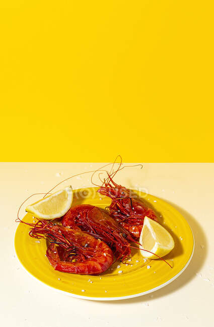 Смачні морепродукти варених червоних креветок зі свіжими скибочками лимона та грубою сіллю на двокольоровому фоні — стокове фото