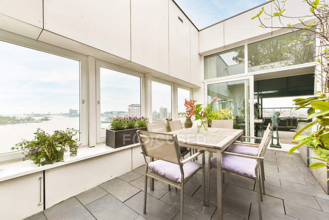 Tisch mit Stuhl auf geräumiger Terrasse mit verschiedenen grünen Pflanzen in Töpfen — Stockfoto