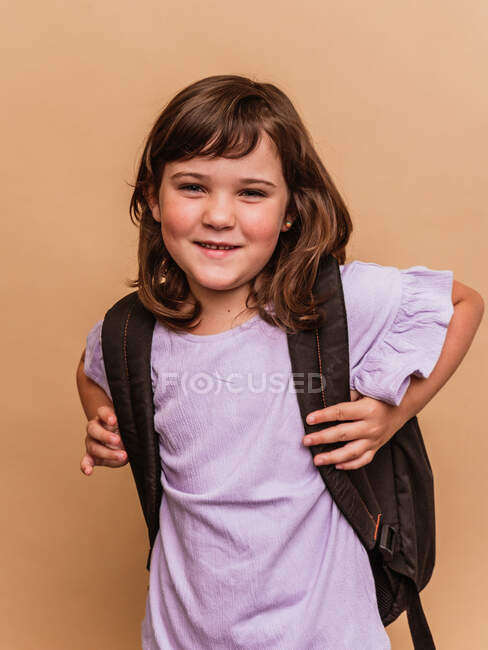 Симпатичный школьник, стоящий на коричневом фоне в студии и смотрящий в камеру — стоковое фото