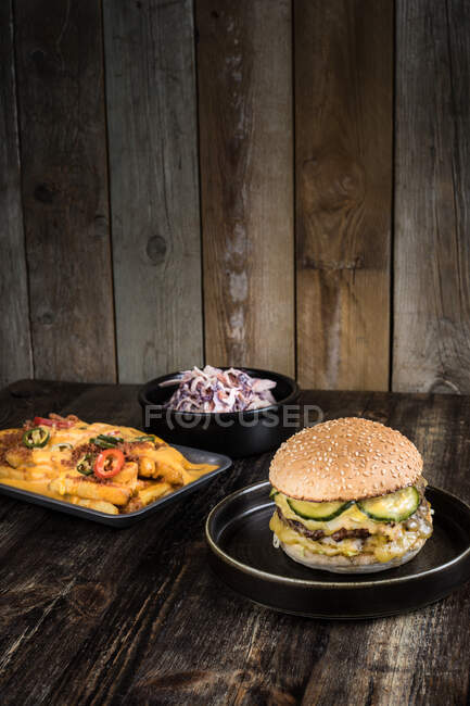 Апетитні бургери з смаженим м'ясом і сиром розміщені поруч з випічкою з сирною картоплею з перцем і мискою з салатом на дерев'яному столі в ресторані — стокове фото