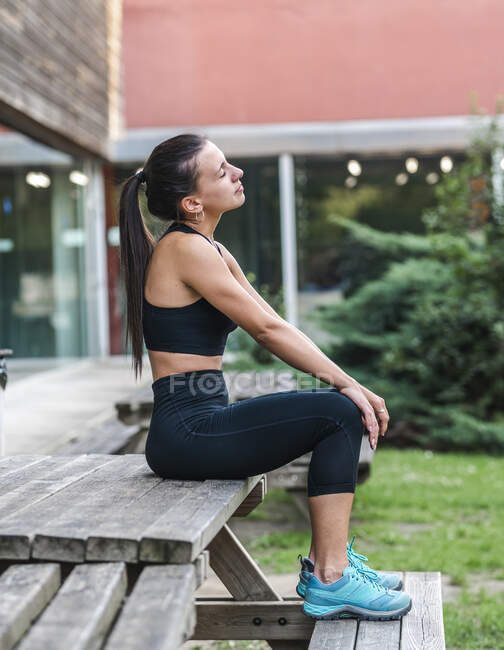 Young sportswoman with closed eyes stretching neck and shoulder while warming up during fitness workout in yard — Stock Photo