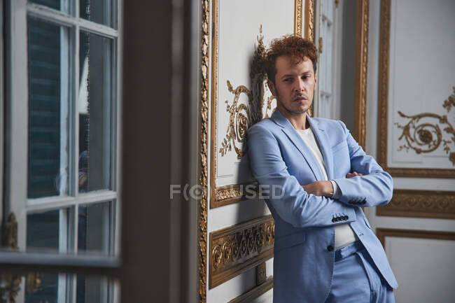 Thoughtful male in suit standing with crossed arms and leaning on wall in posh room — Stock Photo