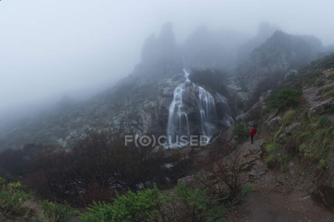Tourist admiring cascades with fast water streams on rough mount under misty sky in autumn — Stock Photo