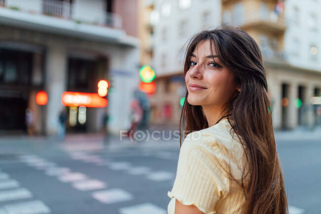 Вид збоку молодої ніжної жінки дивиться на камеру на міську вулицю в м'якому сонячному світлі — стокове фото