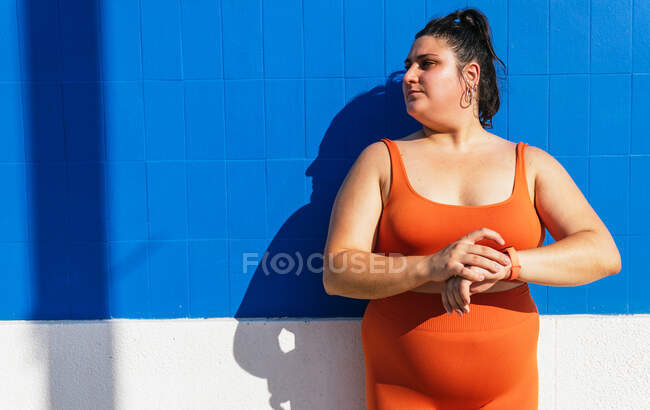 Sportswoman with curvy body with heart rate on wearable tracker during workout on street while looking away — Stock Photo