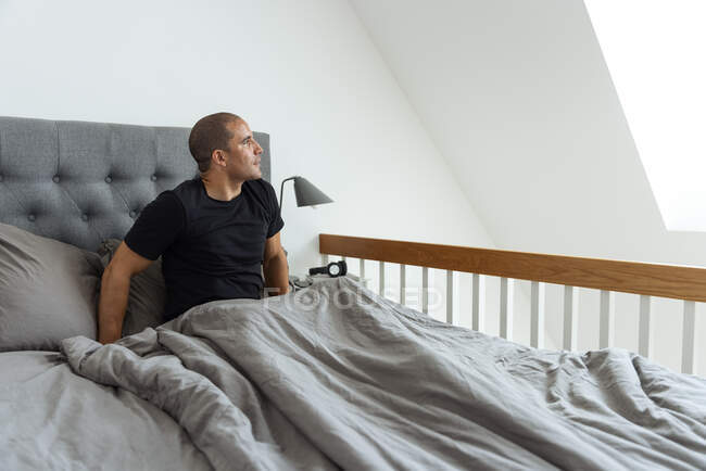 Sorglose Männchen sitzen auf dem Bett und genießen den Morgen, wenn sie zu Hause wegschauen — Stockfoto