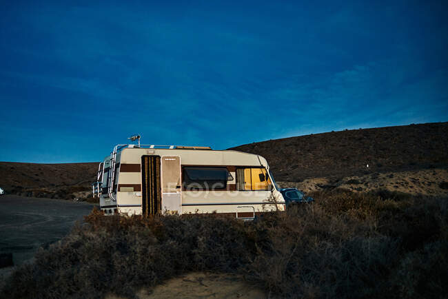 Camper vintage com porta aberta estacionada perto de colinas contra o céu azul à noite em Fuerteventura, Espanha — Fotografia de Stock