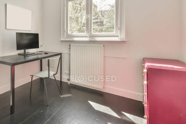 Простий стіл з комп'ютерним монітором і стільцем розміщений біля стіни з порожньою макетною рамою в маленькому мінімалістичному стилі кімнаті з шафою в сучасній квартирі — стокове фото