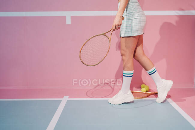 Вид сбоку на урожай неузнаваемая стильная спортсменка в коленных носках с теннисной ракеткой прогуливающаяся по спортивной площадке — стоковое фото
