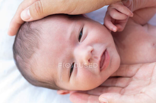 Closeup of crop anonymous mother touching head of cute infant smiling and looking at camera — Stock Photo
