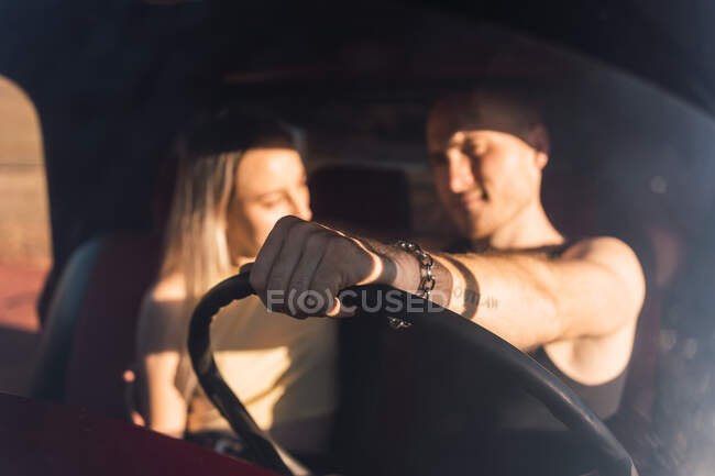 Крутий хлопець сидить в машині з холодною дівчиною в сонячний день — стокове фото