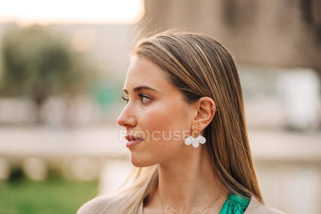 Gentle female in trendy earrings and stylish outfit looking away in city — Stock Photo