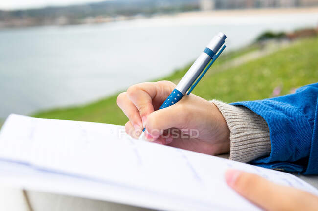Anonyme écriture féminine avec un stylo bleu dans un bloc-notes tout près de la mer — Photo de stock