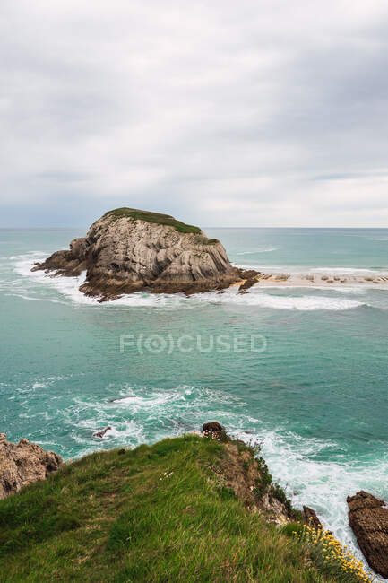 Paisaje fascinante con pequeña península rocosa y playa de arena bañada por agua de mar turquesa espumosa en Liencres Cantabria España - foto de stock