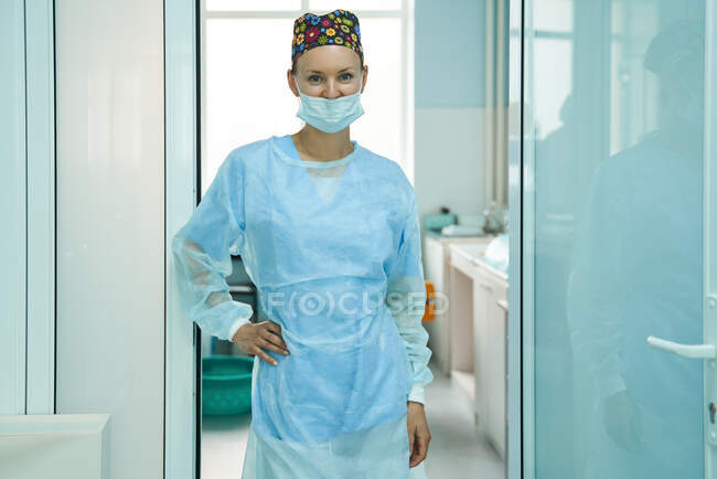 Cheerful adult female medic in sterile mask and ornamental cap looking at camera in hospital — Stock Photo