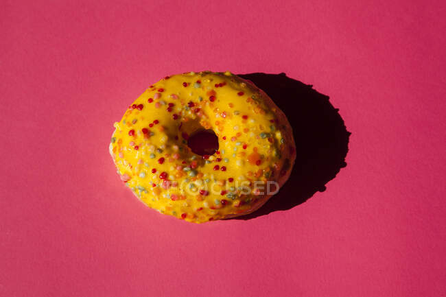 Vista dall'alto di una ciambella ricoperta di zucchero giallo con palline colorate su sfondo rosa — Foto stock