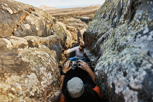 Анонімний мандрівник стріляє в друга через смартфон, стоячи у вузькій щілині між грубими скелями у сільській місцевості Фуертевентура (Іспанія). — стокове фото