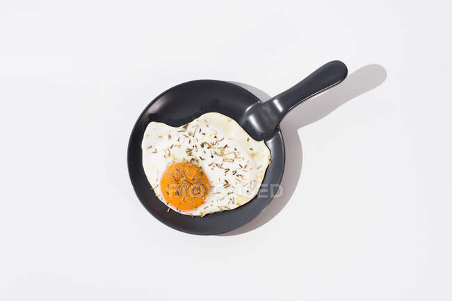 Смачне смажене яйце на чорній сковороді, що подається на столі на білому тлі в студії — стокове фото
