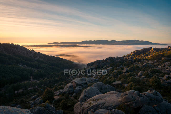 Vista panorámica de Pedriza con niebla que se difunde entre la cordillera de Guadarrama y rocas con coníferas al amanecer en España - foto de stock