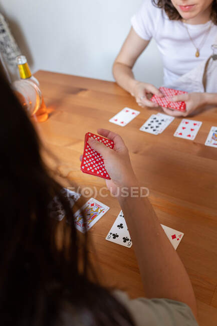 Свыше анонимные восторженные ЛГБТ-пара женщин, сидящих за столом и играющих в карты во время развлечений в выходные дни дома — стоковое фото