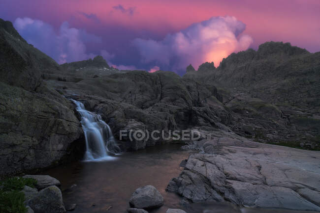 Vista panorâmica de Sierra de Gredos com cascata e lagoa com fluidos de água espumosos sob céu nublado ao pôr-do-sol — Fotografia de Stock
