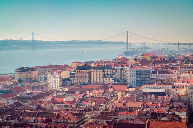 Vista del dron de edificios techados rojos ubicados en la costa del río Tajo no lejos del puente 25 de Abril en la mañana en Lisboa, Portugal - foto de stock