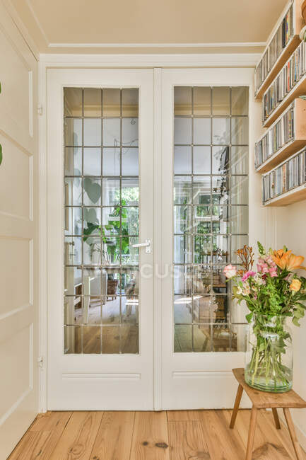 Vaso com flores colocadas no banco sob estantes na frente da porta de vidro branco no corredor elegante — Fotografia de Stock