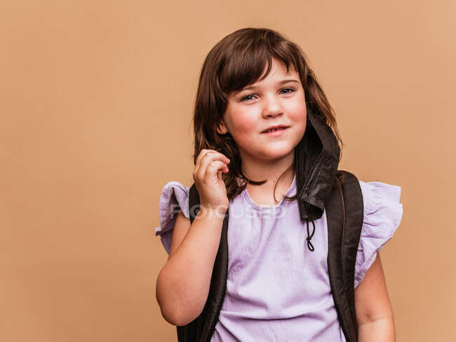 Delighted kid with rucksack and taking off the mask from coronavirus on brown background in studio — Stock Photo