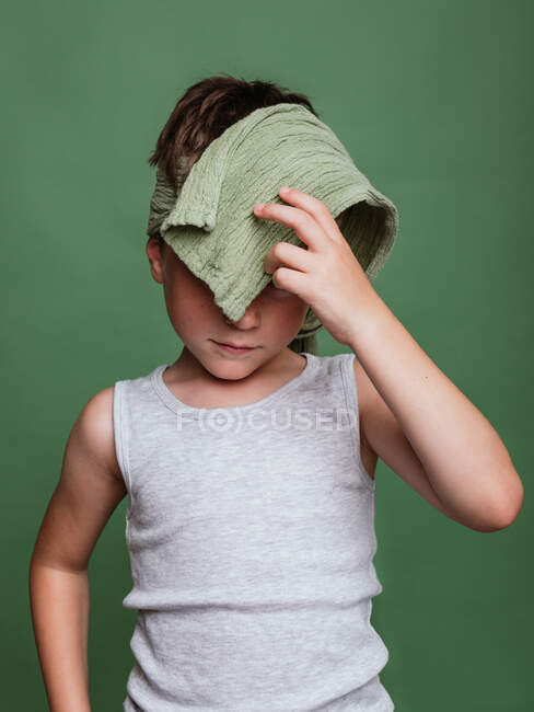 Сором'язлива карате дитина в хедзімакі покриває обличчя на зеленому фоні в студії — стокове фото