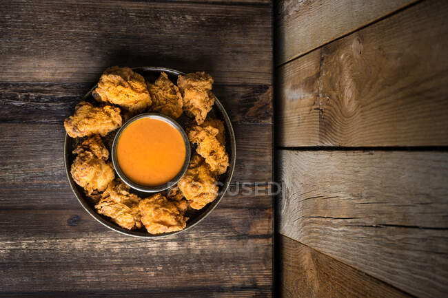 De cima de frango crocante frito saboroso e molho servido em placa redonda na mesa de madeira perto da parede — Fotografia de Stock