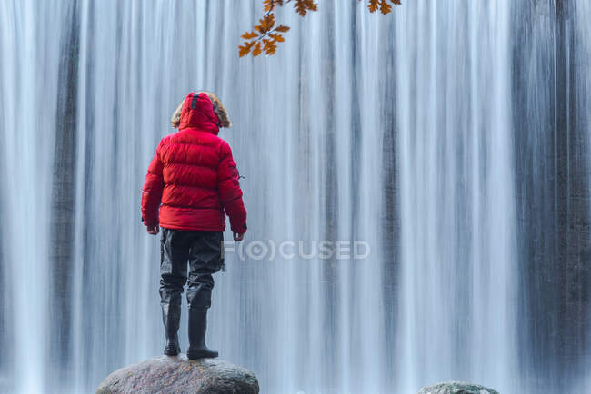 Вид на путешествующего мужчину в теплой одежде, стоящего на валуне и любующегося видом на быстрый водопад на реке Лозоя в Национальном парке Гуадарама — стоковое фото