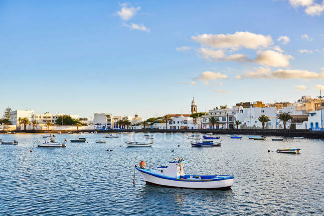 Muitos barcos flutuando em águas fluviais ondulantes perto da cidade contra o céu azul nublado em Fuerteventura, Espanha — Fotografia de Stock
