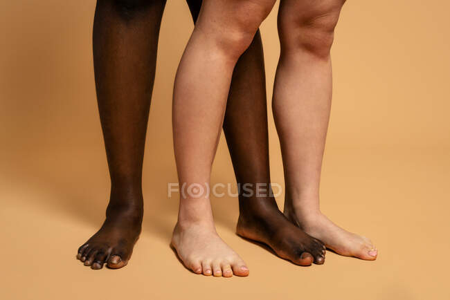 Nicht wiederzuerkennende multiethnische barfüßige Weibchen stehen dicht an dicht auf beigem Hintergrund im Studio für Body-Positivity-Konzept — Stockfoto