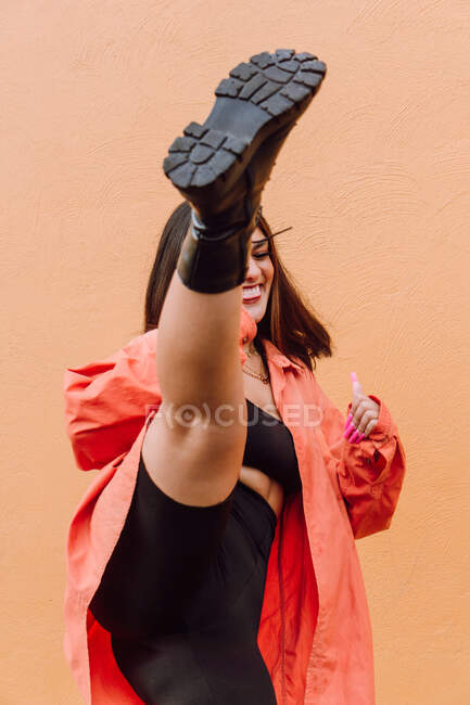 Joyeux millénium féminin en tenue élégante coup de pied air contre le mur orange — Photo de stock
