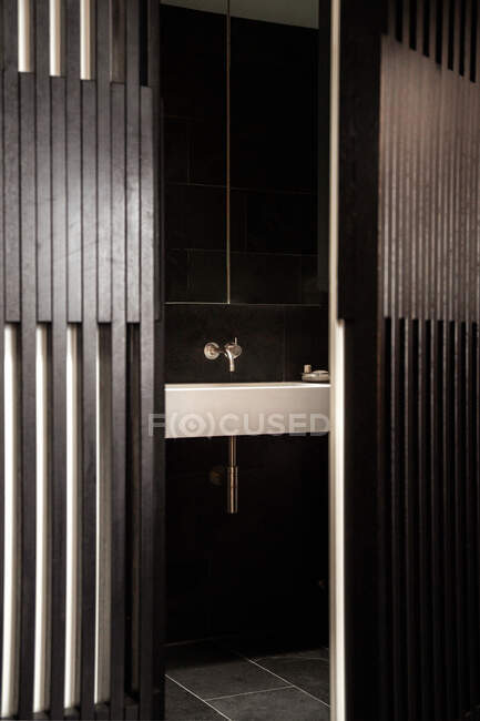 Par la porte de l'évier blanc dans la salle de bain contemporaine avec des murs carrelés noirs et le sol — Photo de stock