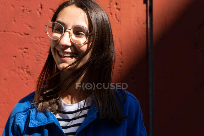 Positive Frau in stylischem Outfit blickt an einem sonnigen Tag in der Stadtstraße auf den bunten Hintergrund einer Hauswand — Stockfoto