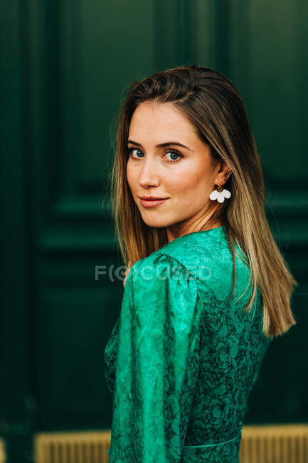 Fröhliche Frau in stilvollem grünem Kleid steht neben dekorativen Holztüren auf der Straße und blickt in die Kamera — Stockfoto