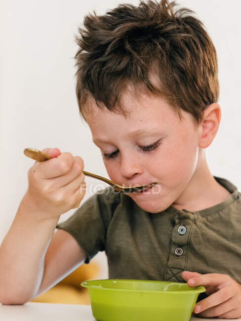 Adorabile ragazzo mangiare zuppa di panna appetitosa con cucchiaio durante il pranzo a casa — Foto stock
