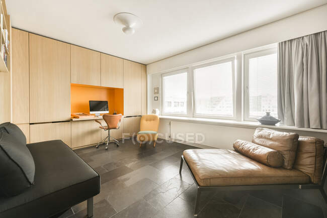 Простора робоча кімната з сучасними диванами та столом з комп'ютерним монітором у квартирі, спроектованій в мінімальному стилі — стокове фото