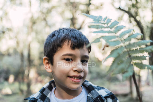 Bambino focalizzato con foglia di pianta verde che guarda la fotocamera nei boschi su sfondo sfocato — Foto stock