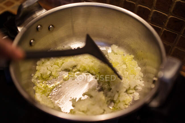 Dall'alto del raccolto irriconoscibile chef friggere aglio tritato e cipolla in padella metallica durante la cottura del cibo in cucina a casa — Foto stock
