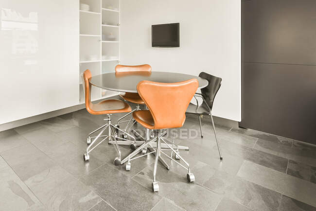 Круглий стіл і стільці розміщені в сучасній просторій кімнаті з телевізором, що висить на білій стіні — стокове фото