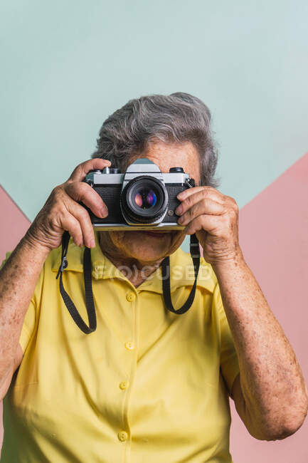 Сучасна літня жінка фотографує старовинну фотокамеру на двокольоровому фоні в студії — стокове фото