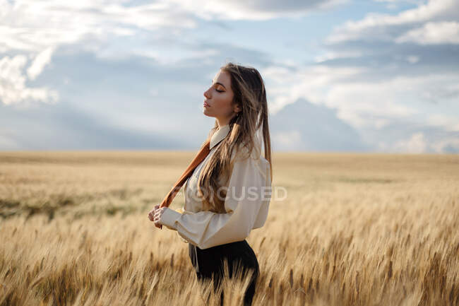 Side view of young mindful female in formal wear with tie and closed eyes among spikes in countryside — Stock Photo