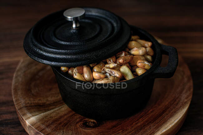 High angle of heap of cereal grain in black saucepan with lid placed on wooden board on table in kitchen — Stock Photo